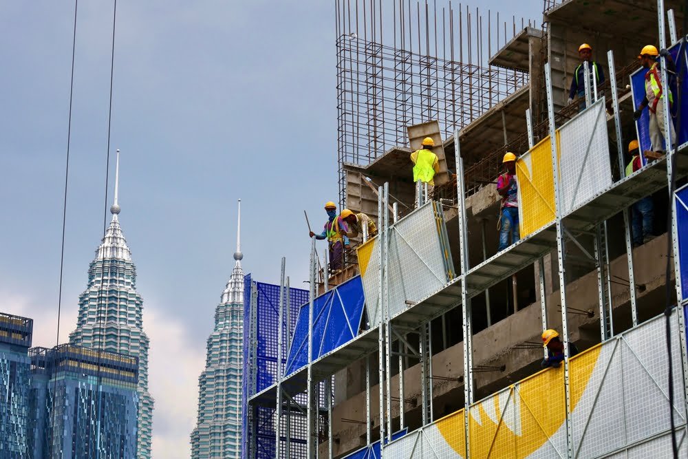 Construction site in Malaysia featuring workers on scaffolding, actively engaged in building and renovation tasks.