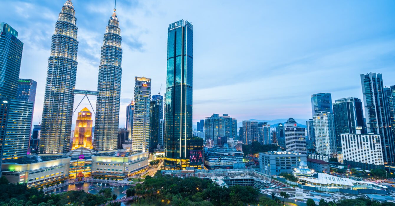 Twilight cityscape with illuminated skyscrapers and park in Kuala Lumpur, showing the growth of Urbanization in Malaysia Construction raise the infrastructure demand.