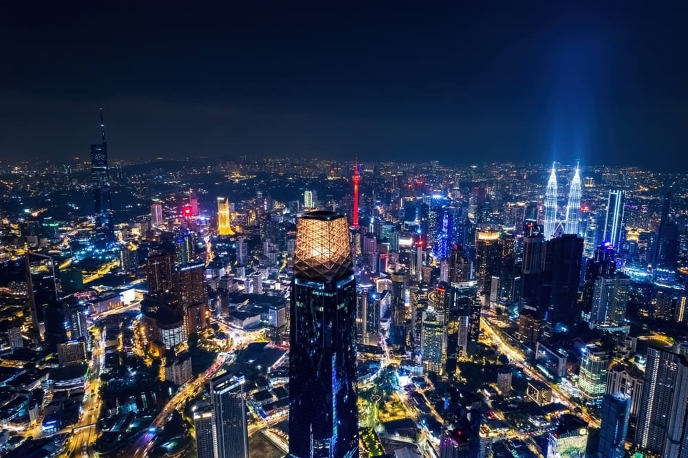 A nighttime aerial view of a brightly lit Kuala Lumpur cityscape with dense skyscrapers, indicating the Public-Private Partnerships Malaysia.