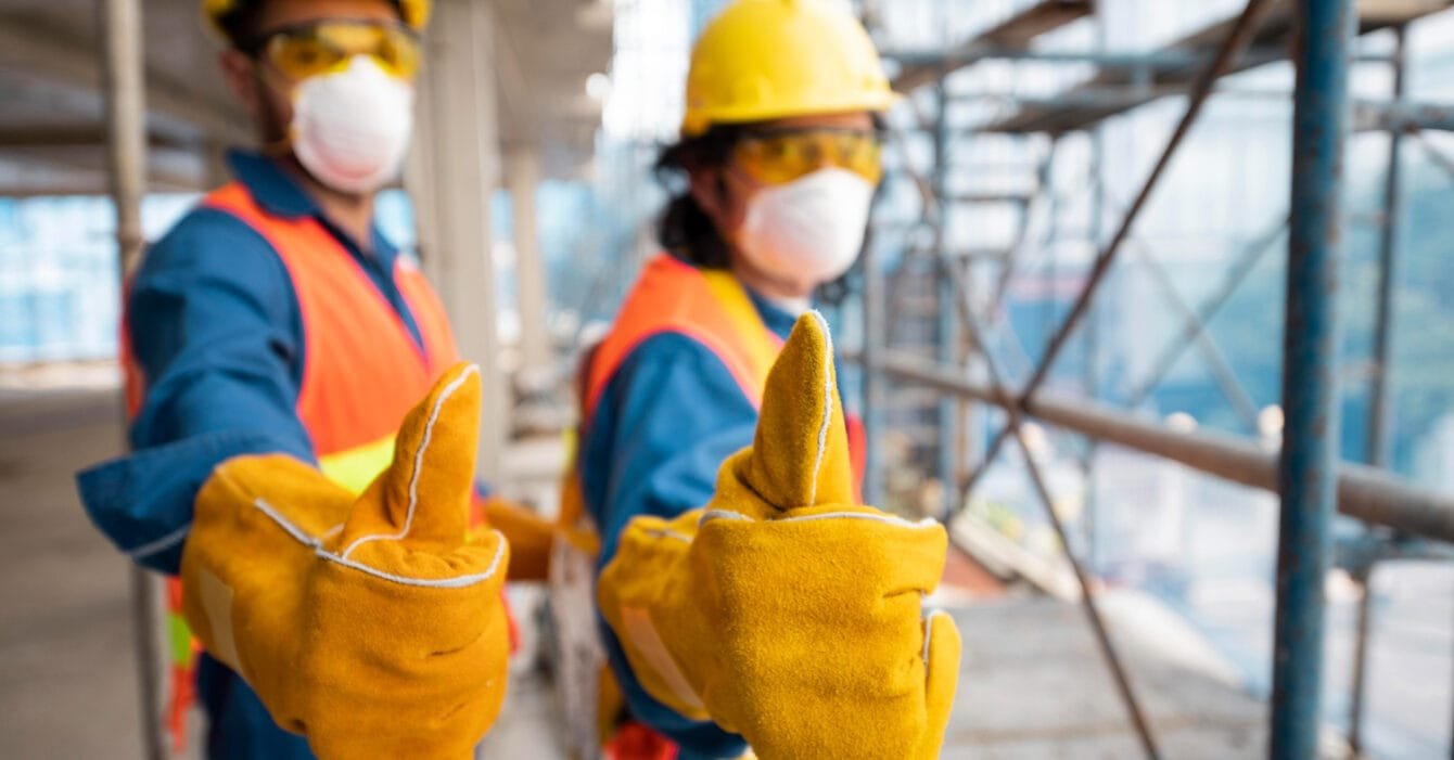 Two construction workers in safety gear giving thumbs up on a site, representing Construction Safety in Malaysia.