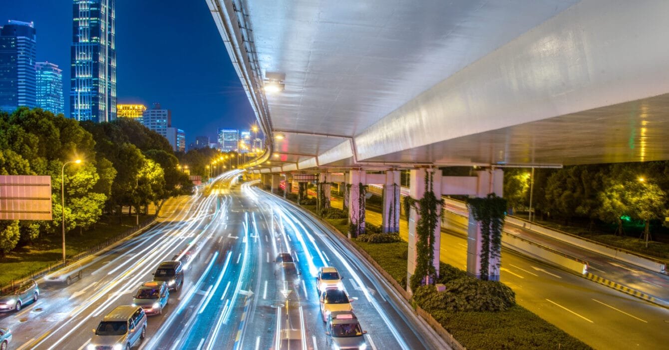 A night cityscape with light trails on a busy road under an overpass and illuminated skyscrapers in the background, representing successful PPP Projects Malaysia.