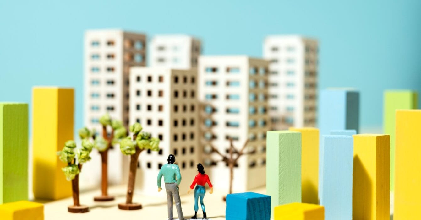 Malaysia Urbanization Growth: Miniature figures of people in a conceptual cityscape with colorful block buildings and trees.