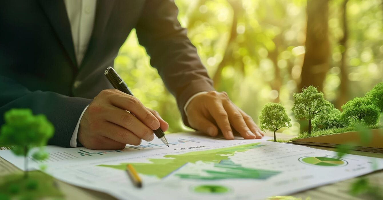 Malaysia Green Building Certifications: A business professional in a suit signs documents featuring green graphs, surrounded by miniature trees, symbolizing sustainability efforts.